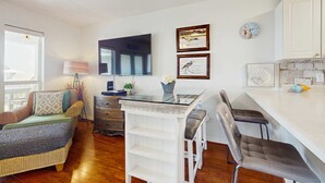 A cozy living room with a sofa, a glass-top coffee table, and a dining area with a white table and chairs. - Fourth-floor, Caribbean corner condo with ocean views, pool, & hot tub (Santa Rosa Beach)