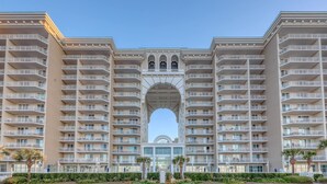 Ein mehrstöckiges Hotel mit einem zentralen Bogen, Balkonen und einem gepflegten Garten.