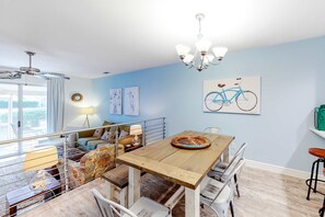 Ein Essbereich mit Holztisch, Stühlen und einer Chandelieber. Im Hintergrund befinden sich ein Sofa und eine Lampe.