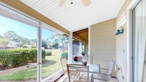 A covered patio with a table and chairs, large windows, and a view of the backyard. - Beautiful gem at Bayou Village, golf cart, WiFi, & resort pools (Miramar Beach)