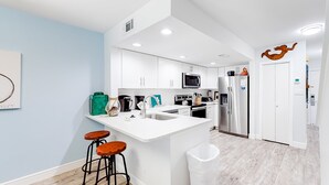 A modern kitchen with white cabinets, a central island with stools, stainless steel appliances, and a wooden floor. - Beautiful gem at Bayou Village, golf cart, WiFi, & resort pools (Miramar Beach)