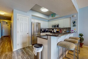 A modern kitchen with white cabinets, stainless steel appliances, and a bar area with stools. - Majestic Sun B513 | Beachfront Condo with Pool! (Miramar Beach)