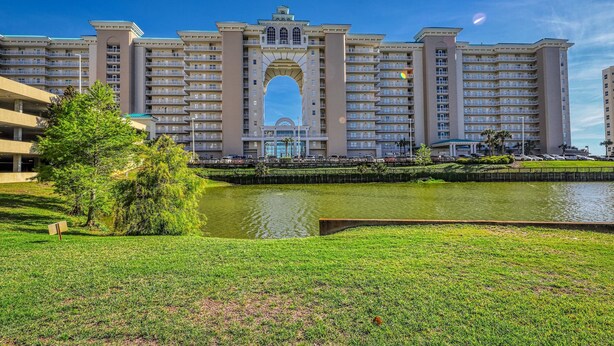 Um hotel grande com um arco central, várias varandas e um corpo d'água à frente.