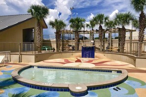 A swimming pool with a colorful tile design, surrounded by palm trees and a covered area with a roof. - Ocean-view condo with pools & hot tub, balcony, central AC, W/D (Miramar Beach)