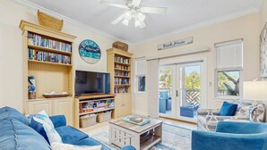 A living room with a blue sofa, a coffee table, a bookshelf, a television, and a sign that reads "Beach House". - Cozy coastal condo with shared pool,  beach access and Wifi (Santa Rosa Beach)