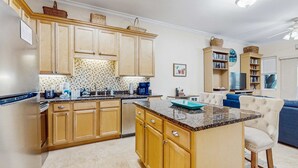 A modern kitchen with wooden cabinets, a granite countertop, and a central island. - Cozy coastal condo with shared pool,  beach access and Wifi (Santa Rosa Beach)