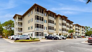 A multi-story residential building with balconies, a parking lot, and a clear sky. - Cozy coastal condo with shared pool,  beach access and Wifi (Santa Rosa Beach)