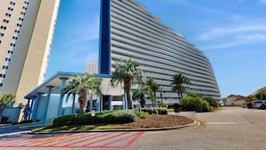 A modern hotel with a curved facade, multiple floors, and a prominent vertical blue stripe. - Gulf-view resort condo with pools, hot tubs, balcony, WiFi, W&D, & AC (Miramar Beach)