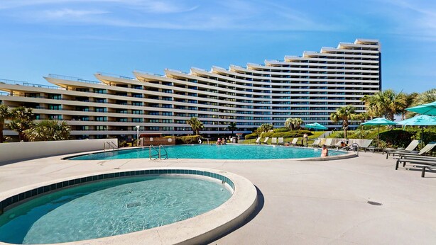 A hotel with multiple swimming pools, a large building with balconies, and palm trees. - Gulf-view resort condo with pools, hot tubs, balcony, WiFi, W&D, & AC (Miramar Beach)