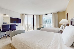 A hotel room with a large bed, a desk with a computer, a chair, and a view of the city. - Gulf-view condo with beach access, pools, hot tubs, tennis, & private balcony (Miramar Beach)