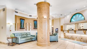 A lobby with a large central column, a reception desk, a blue sofa, and a decorative wall with abstract art.