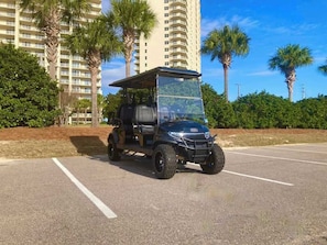 Ein Golfwagen steht auf einem Parkplatz, im Hintergrund ein Hochhaus und Palmen.