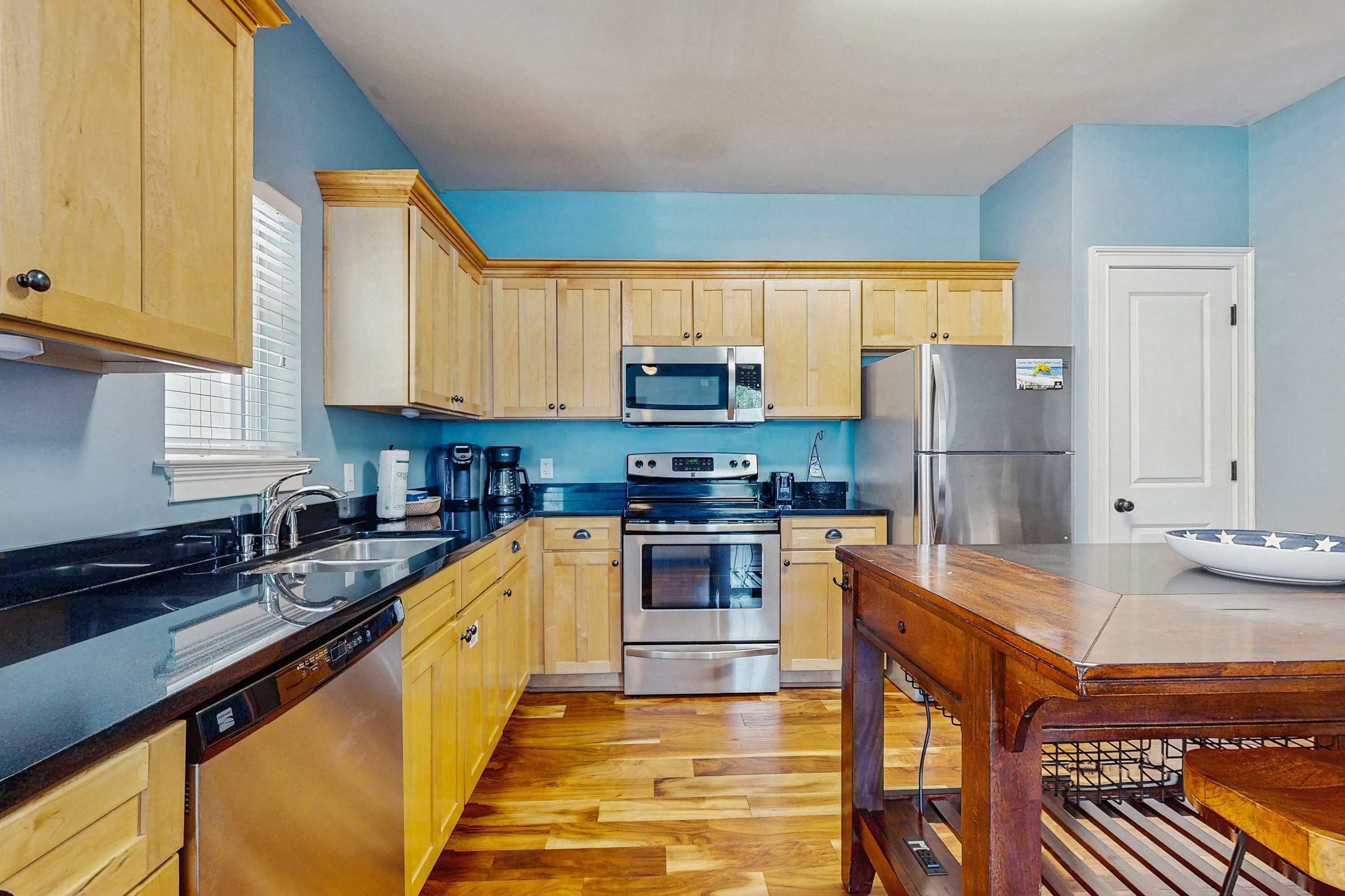 A kitchen with wooden cabinets, a black countertop, stainless steel appliances, and a wooden dining table.