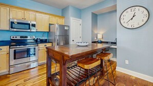 A kitchen with wooden cabinets, stainless steel appliances, a wooden island with stools, and a wall clock. - Dog-friendly coastal haven with premium beach perks & resort indulgence (Santa Rosa Beach)