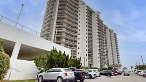A multi-story parking garage adjacent to a high-rise building with balconies. - This cozy and bright resort studio is perfect for a beach getaway. (Miramar Beach)