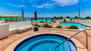 A swimming pool with a view of the ocean, lounge chairs, and umbrellas. - This cozy and bright resort studio is perfect for a beach getaway. (Miramar Beach)