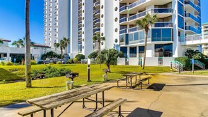 A hotel courtyard with picnic tables, palm trees, and a building with multiple balconies. - This cozy and bright resort studio is perfect for a beach getaway. (Miramar Beach)