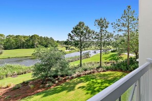 A view from a balcony overlooking a golf course with a pond, trees, and a clear blue sky.