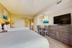 A hotel room with two beds, a dining area, a TV, and a large cabinet.