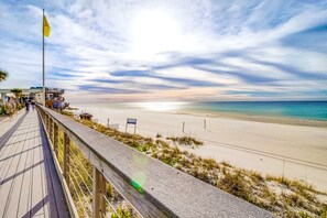 A wooden boardwalk leading to a beach with a flag, a building, and a clear sky.