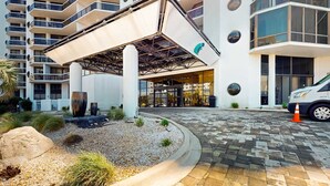 A modern hotel entrance with a covered entrance, large windows, and a parking area. - Cozy condo w/ balcony, beach access & shared pool/hot tub/tennis/gym (Miramar Beach)
