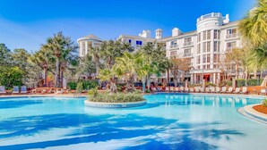 A large pool surrounded by palm trees and a hotel with multiple balconies and a tower. - LaSata beauty with patio, pools, hot tubs, fitness center, AC & beach access (Miramar Beach)