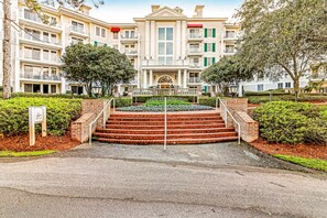 A multi-story hotel with a central entrance, brick steps, and surrounding greenery.