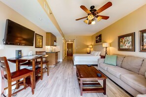 A hotel room with a dining area, a bed, a sofa, a ceiling fan, and artwork on the walls.