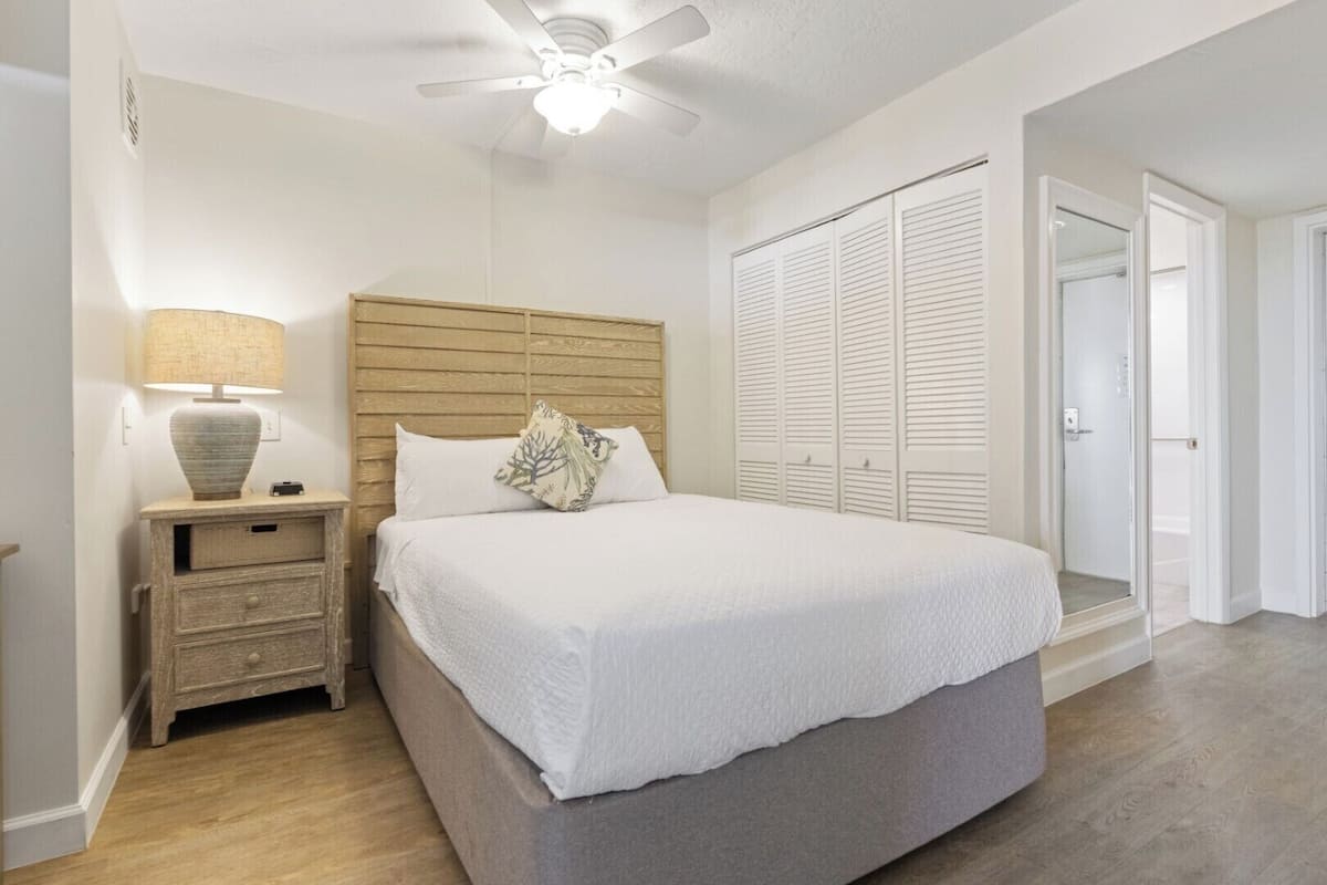 A bedroom with a bed, a nightstand, a lamp, a ceiling fan, and a wardrobe.