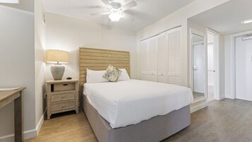 Un dormitorio con cama, mesita de noche, lámpara, ventilador de techo y armario.