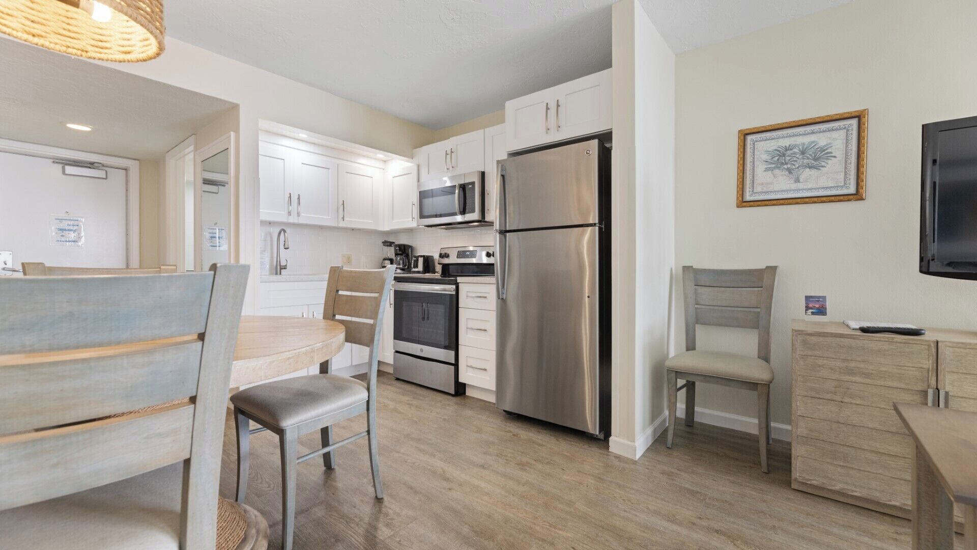 A compact kitchen with white cabinets, stainless steel appliances, and a dining area with a wooden table and chairs.