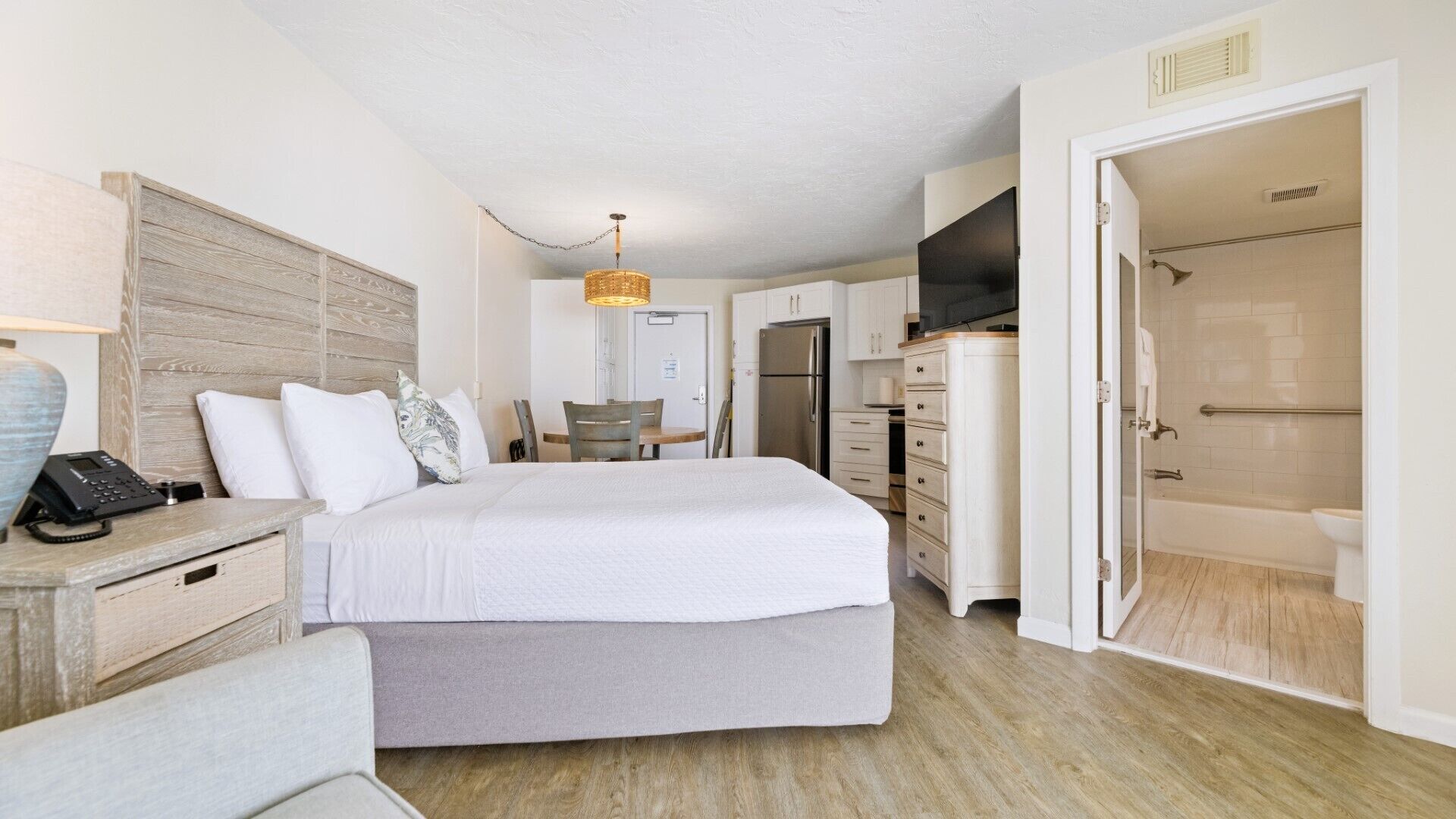 A bedroom with a bed, bedside table, lamp, and a view of the bathroom.