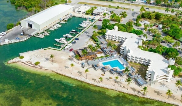 An aerial view of a coastal resort with a marina, a pool area, and beachfront accommodations. - Caloosa Cove Resort by CoolVacay (Islamorada)