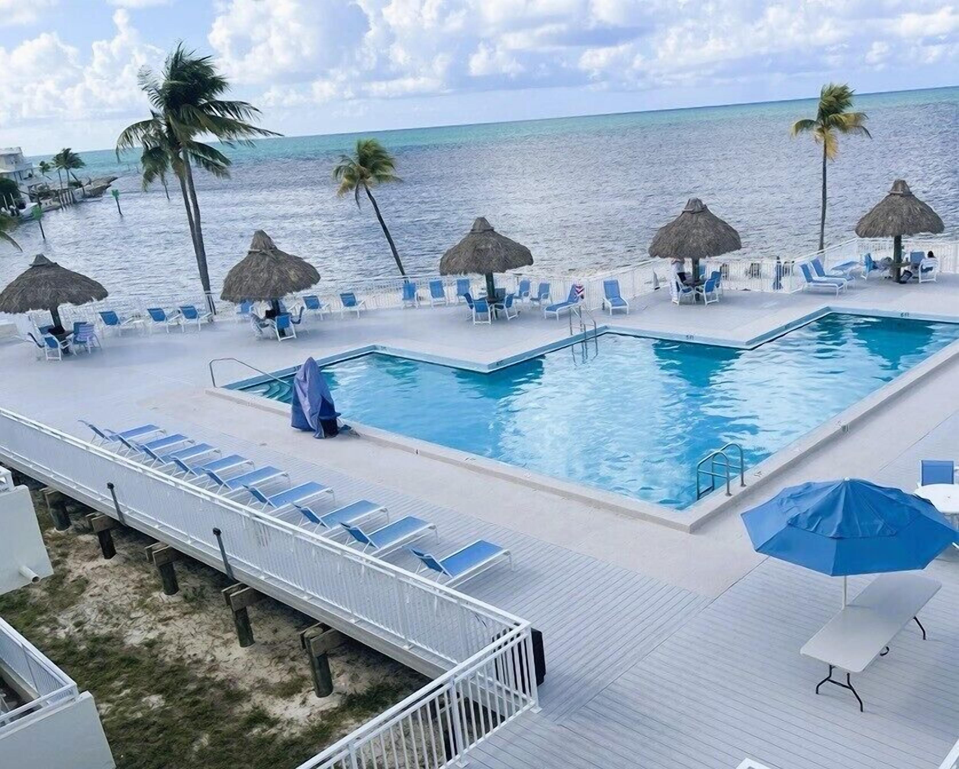 A pool area with lounge chairs and umbrellas, overlooking the ocean.