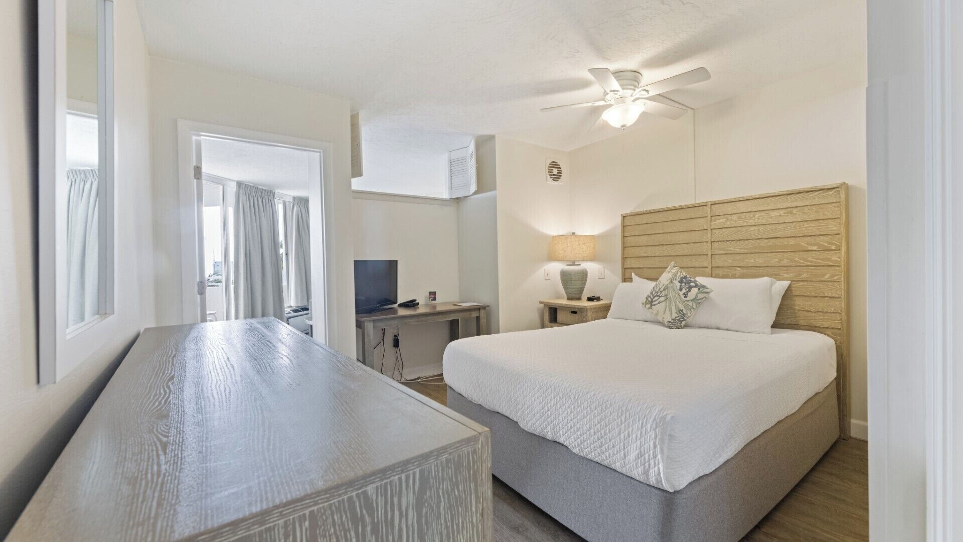 A hotel room with a bed, a desk, a television, a lamp, and a ceiling fan.
