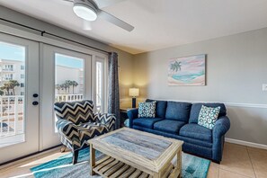 A living room with a blue sofa, patterned armchair, and a wooden coffee table. - Beachfront 2nd floor condo with private balcony, shared pool/hot tub/BBQ (Miramar Beach)