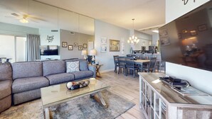 Ein modernes Wohnzimmer mit grauem Sofa, Glastisch und Essbereich mit Holztisch und Stühlen.