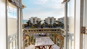 A balcony with a wooden table and chairs, overlooking a street with palm trees and buildings. - Beachy condo with free WiFi & shared pools, hot tub - short walk to the beach (Santa Rosa Beach)
