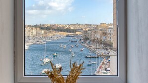 Ein Fenster mit Blick auf einen Hafen, eine Vase mit Trockenpflanzen und ein Holzlegebrett.