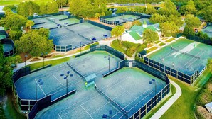An aerial view of a sports complex with multiple tennis courts, surrounded by trees and buildings. - First-floor condo with a kitchen, patio, pool, hot tub, grill, & spa access (Miramar Beach)