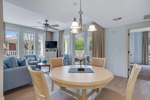 Ein geräumiges Wohnzimmer mit einem runden Esstisch, bequemen Sitzgelegenheiten, einem Deckenventilator und großen Fenstern mit Blick ins Freie.