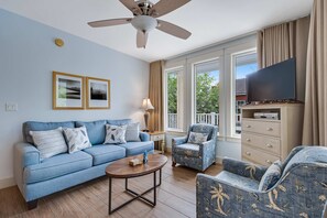 Ein Wohnzimmer mit blauem Sofa, Sesseln, einem Couchtisch, einem Fernseher und einem Deckenventilator.