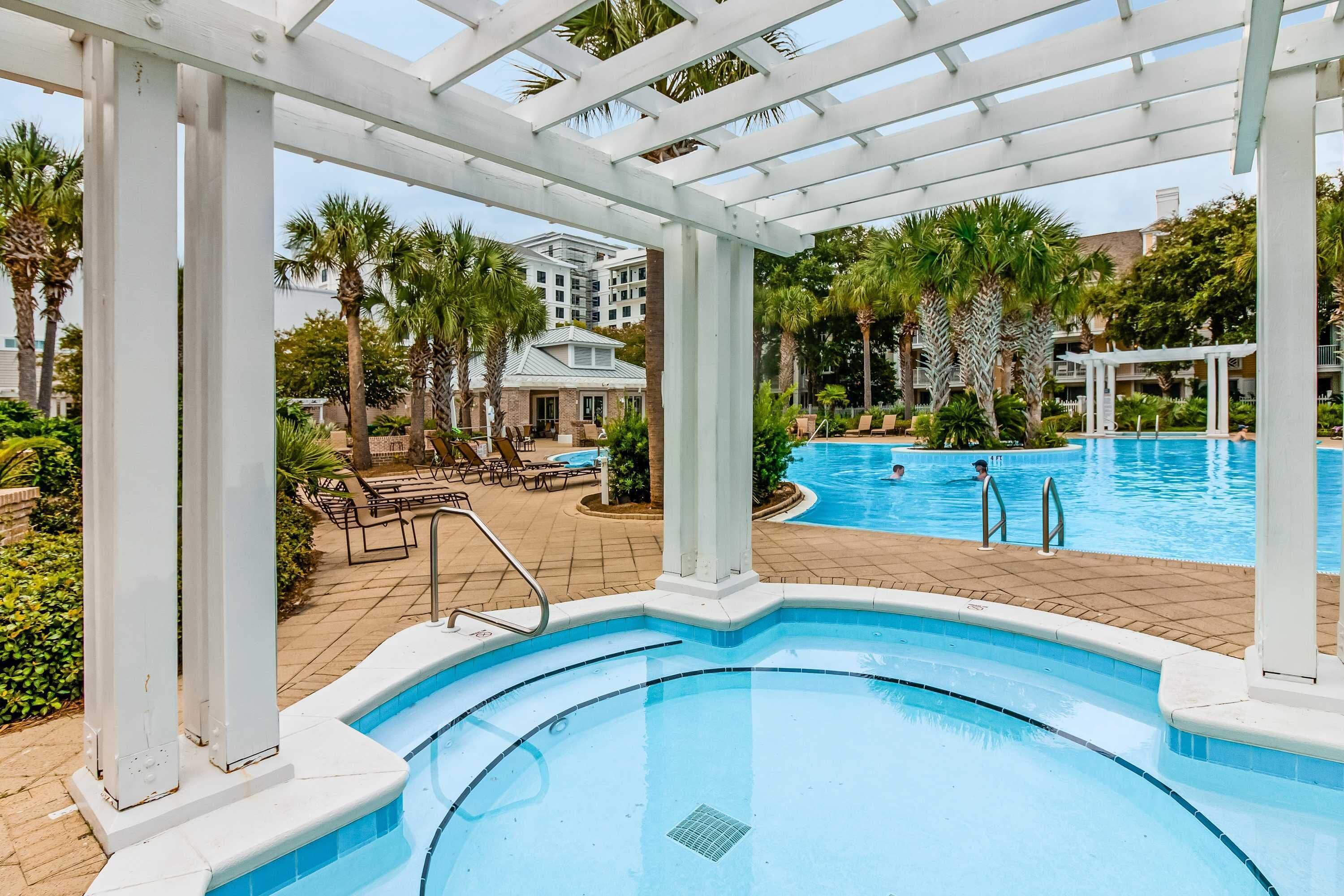 A pool area with a pergola, palm trees, and a building in the background.