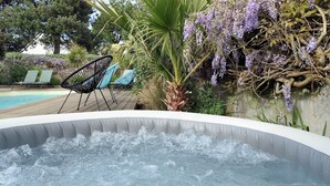 En utomhusbubbelpool omgiven av solstolar och frodig grönska.