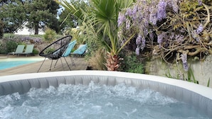 Ein Whirlpool im Freien, umgeben von Liegestühlen und üppiger Bepflanzung.