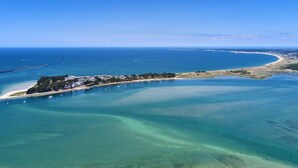 Vogelperspektive einer Küstenlandschaft mit klarem Wasser, einem Sandstrand und einer kleinen Insel mit Gebäuden.