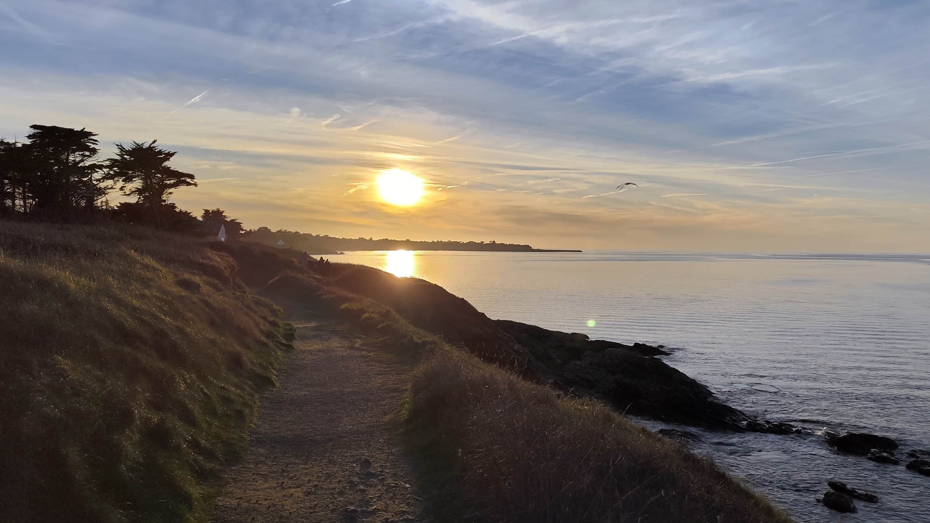 Kyststi med udsigt over havet og en solnedgang.