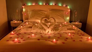 Ein Bett mit Rosenblättern und Kerzen, eine herzförmige Dekoration und ein mit Lichtern versehener Kopfteil.