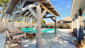 A covered patio area with a grill, outdoor furniture, and a swimming pool. - Coastal Sandy Cay (Miramar Beach)
