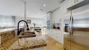 A modern kitchen with granite countertops, stainless steel appliances, and white cabinetry. - Coastal Sandy Cay (Miramar Beach)